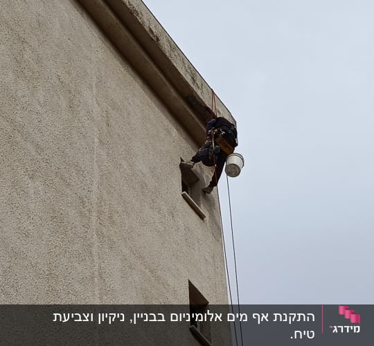 אדם עובד בגובה על קיר בניין עם חבלים